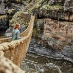 A moment of adventure as a person stands on a suspended bridge over a rugged canyon.