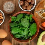 A vibrant flat lay of B12-rich superfoods, including salmon, eggs, dairy products, clams, sardines, beef liver, fortified nutritional yeast, and leafy greens, arranged on a rustic wooden table. The ingredients are fresh and colorful, representing optimal sources of Vitamin B12.